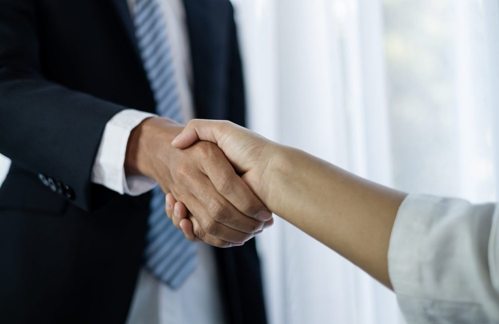 The businessmen and businesswoman shake hands after the meeting was successful and agreed upon.